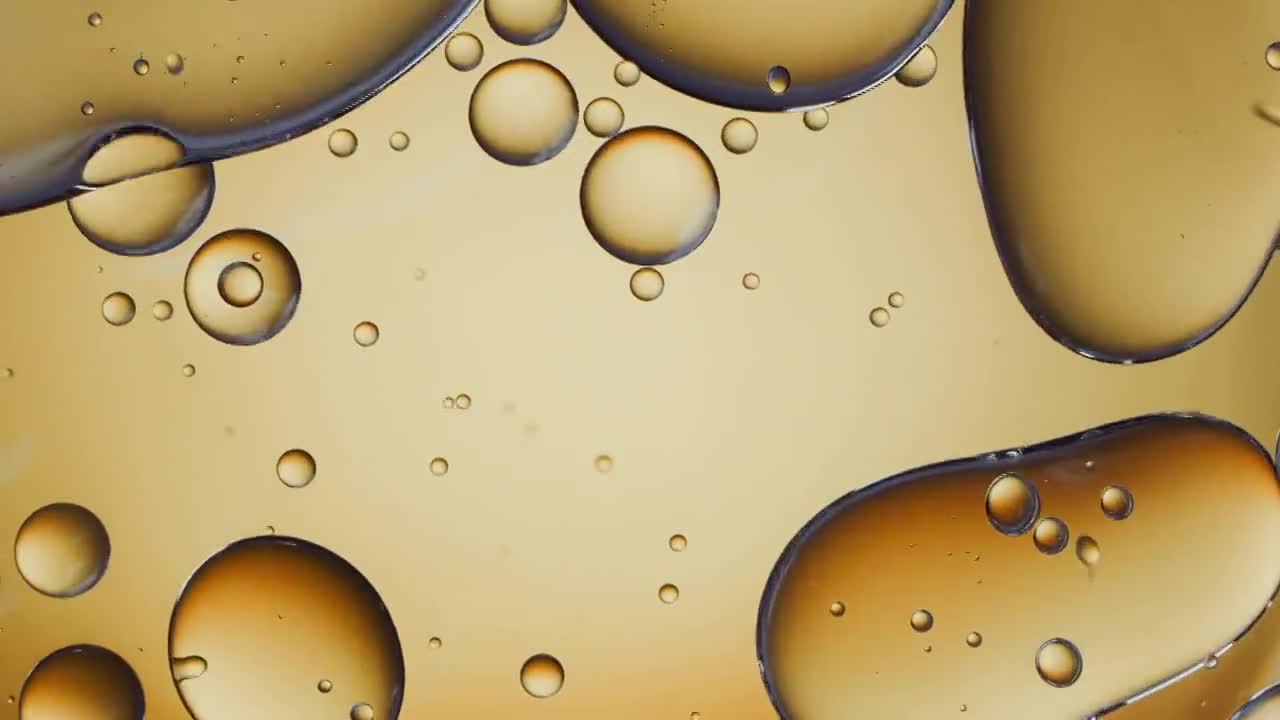 近距離和緩慢運動的頭頂視圖，倒清楚的油到一個池的水和填補浮動油滴的框架在背光金色的背景視頻素材