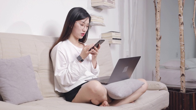 坐在沙发上的亚洲美女，一边用电脑，一边用手机视频下载