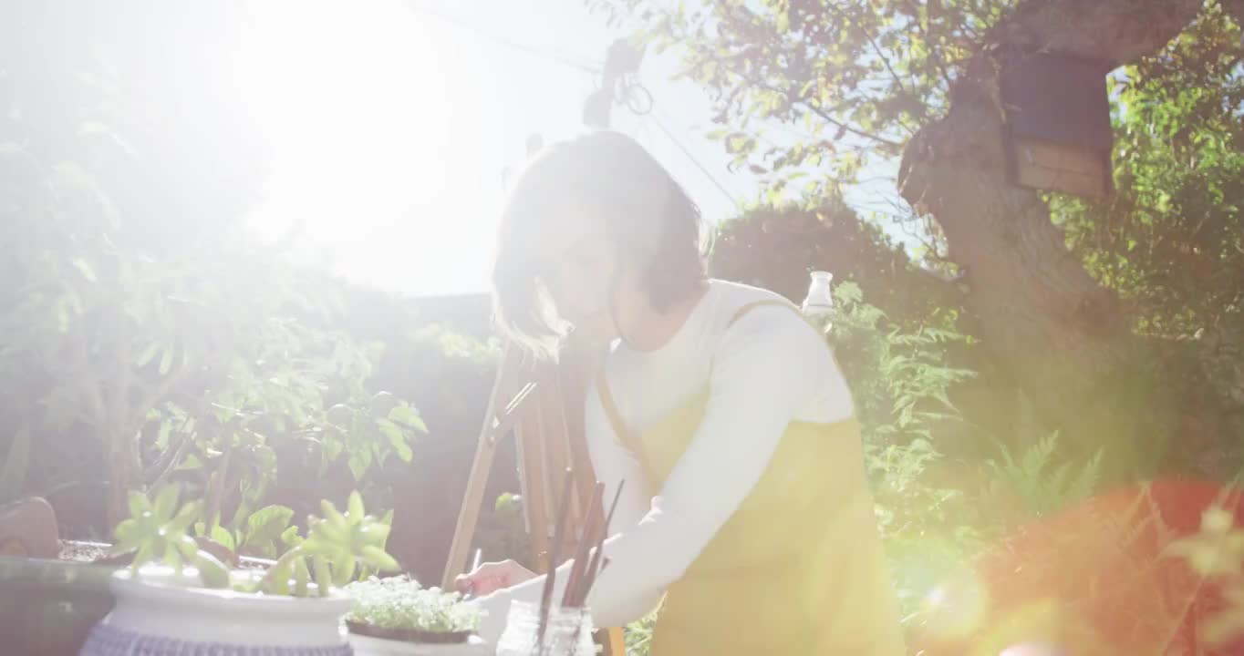 一个棕色头发的白人女人在阳光花园画画视频素材