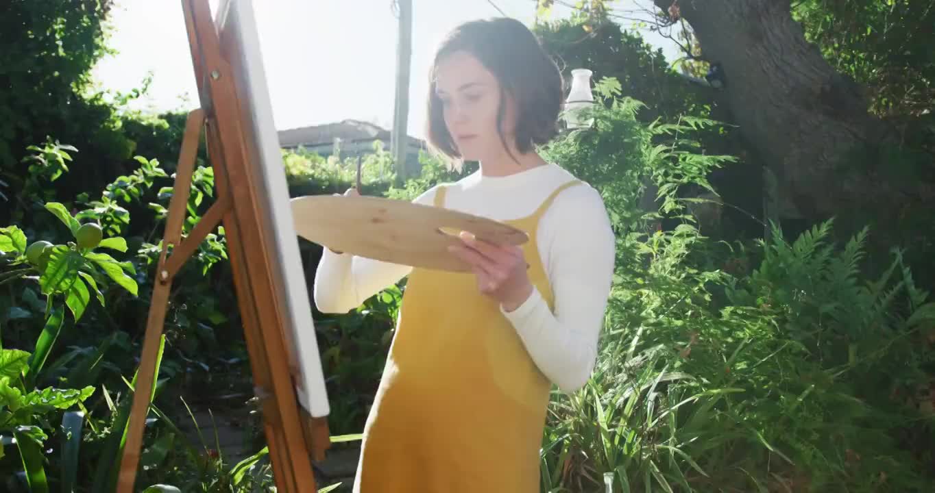 一个棕色头发的白人女人在阳光花园画画视频素材