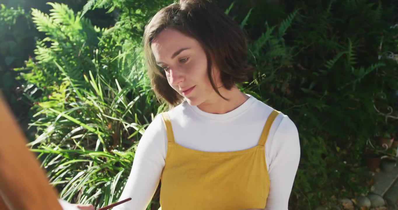 一个棕色头发的微笑白人妇女在阳光花园作画视频素材