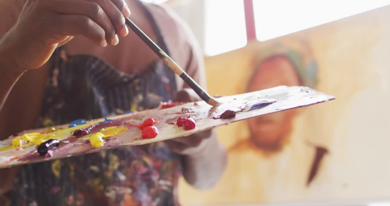 男艺术家身穿围裙，在画室里用笔刷在调色板上调色视频下载