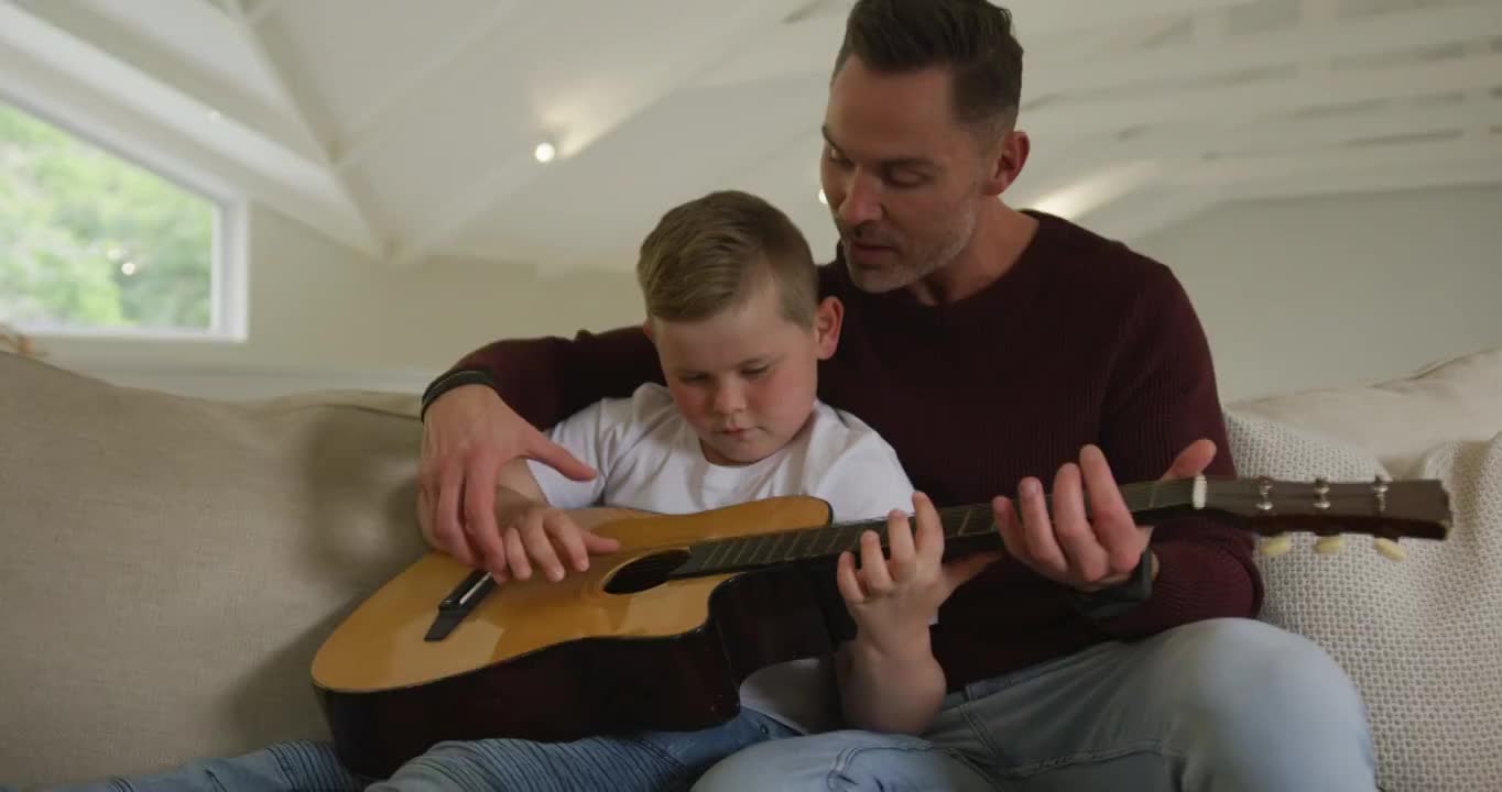白人父亲和儿子一起坐在客厅弹吉他视频购买
