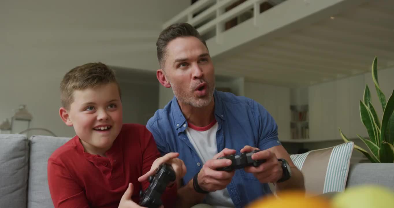 快乐的白人父亲带着儿子坐在客厅玩电子游戏视频购买