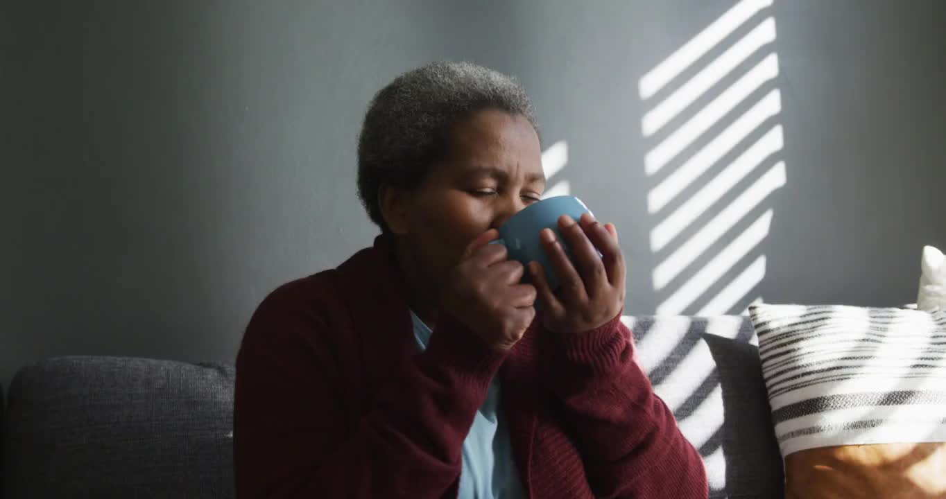 一位沉思的非洲裔美国老妇人一边喝着咖啡，一边望着远方视频素材