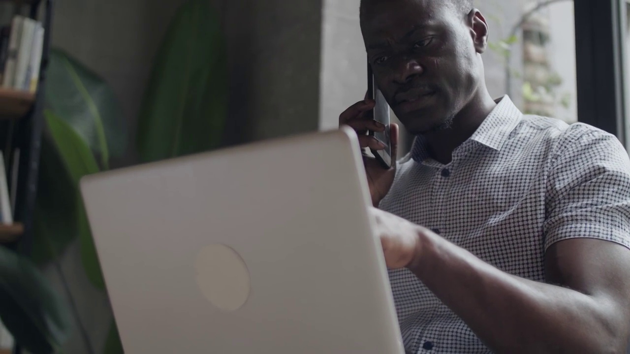一名黑人男子在办公室使用笔记本电脑的特写镜头非洲男子在手机上视频素材