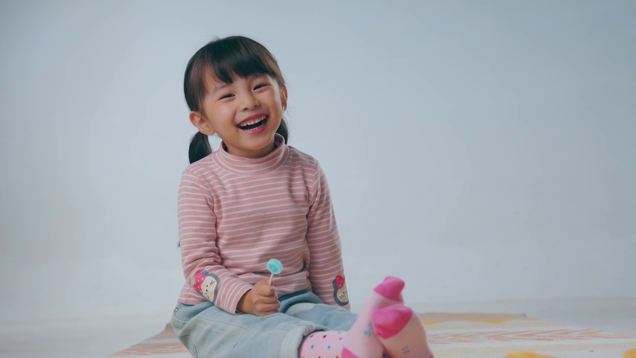 快樂的小女孩坐在地毯上吃棒棒糖視頻購買