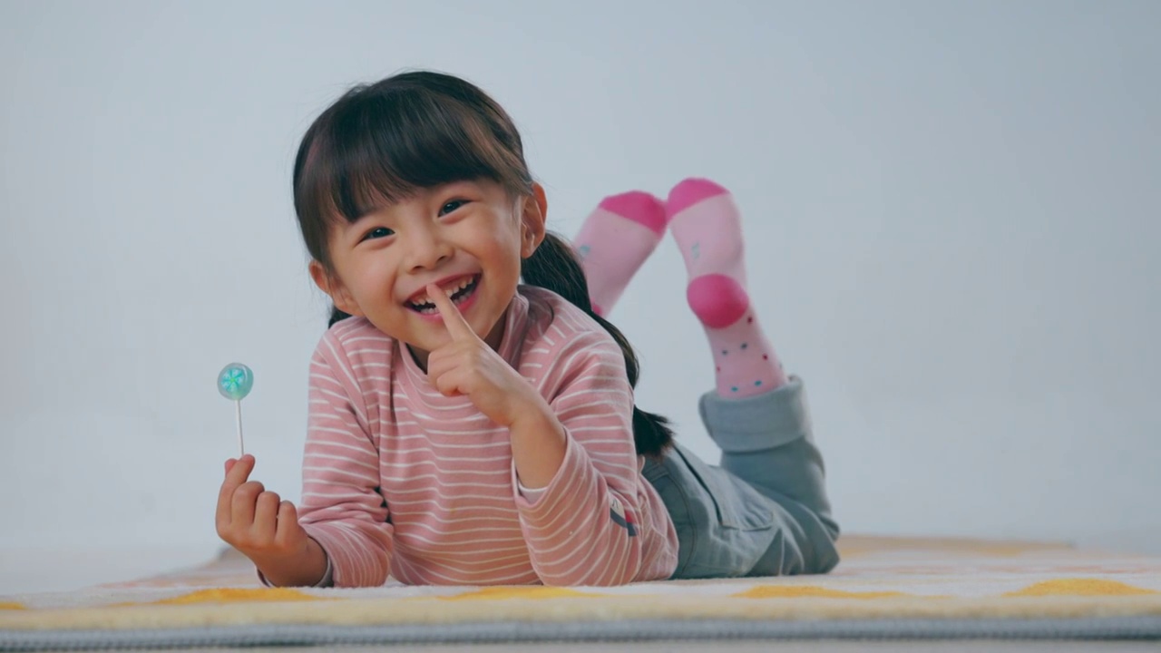 快樂的小女孩趴在地毯上吃棒棒糖視頻購買