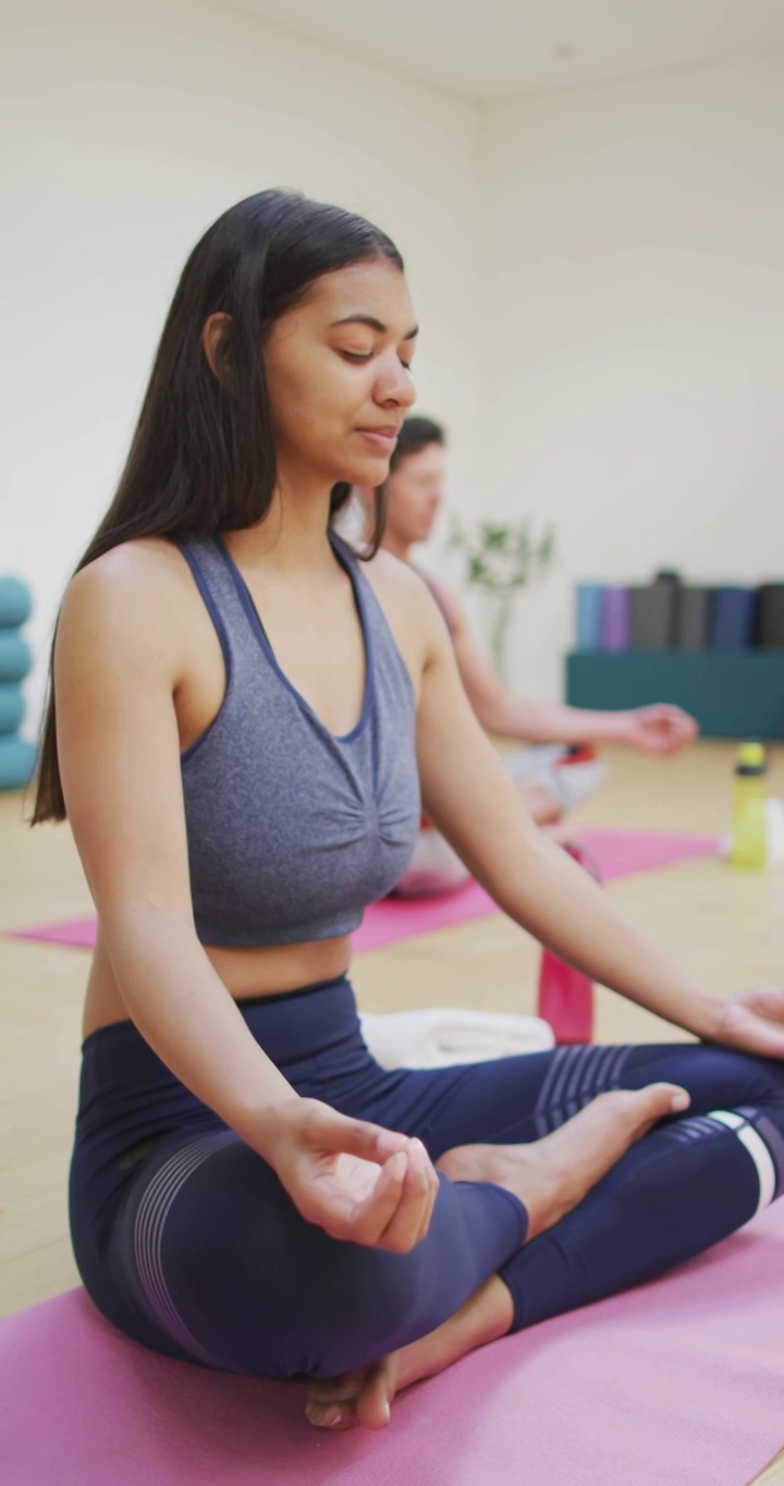 一个黑白混血的女人在瑜伽课上闭着眼睛，双腿交叉冥想的垂直视频视频下载