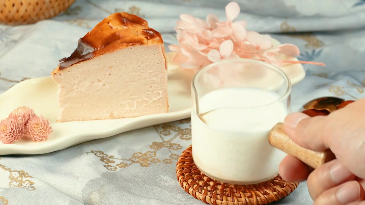 一片精美的芝士蛋糕静静地躺在细瓷盘上一杯牛奶摆放在餐垫上，芝士蛋糕质地柔软细腻充满浓郁奶香淡淡的甜味视频下载