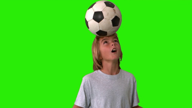 一个小男孩在绿色屏幕上用慢镜头顶球踢足球视频下载