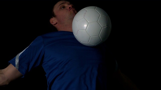 足球运动员控制球与他的胸部在黑色背景的慢动作视频下载