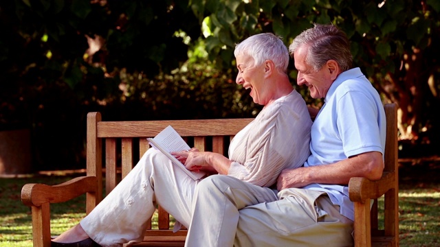 一对老夫妇坐在公园长椅上看书特写视频下载