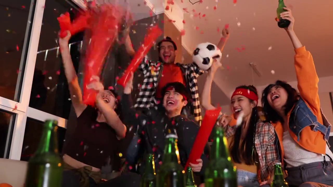 快乐的年轻人在客厅观看足球比赛:欢呼呐喊庆祝胜利视频素材