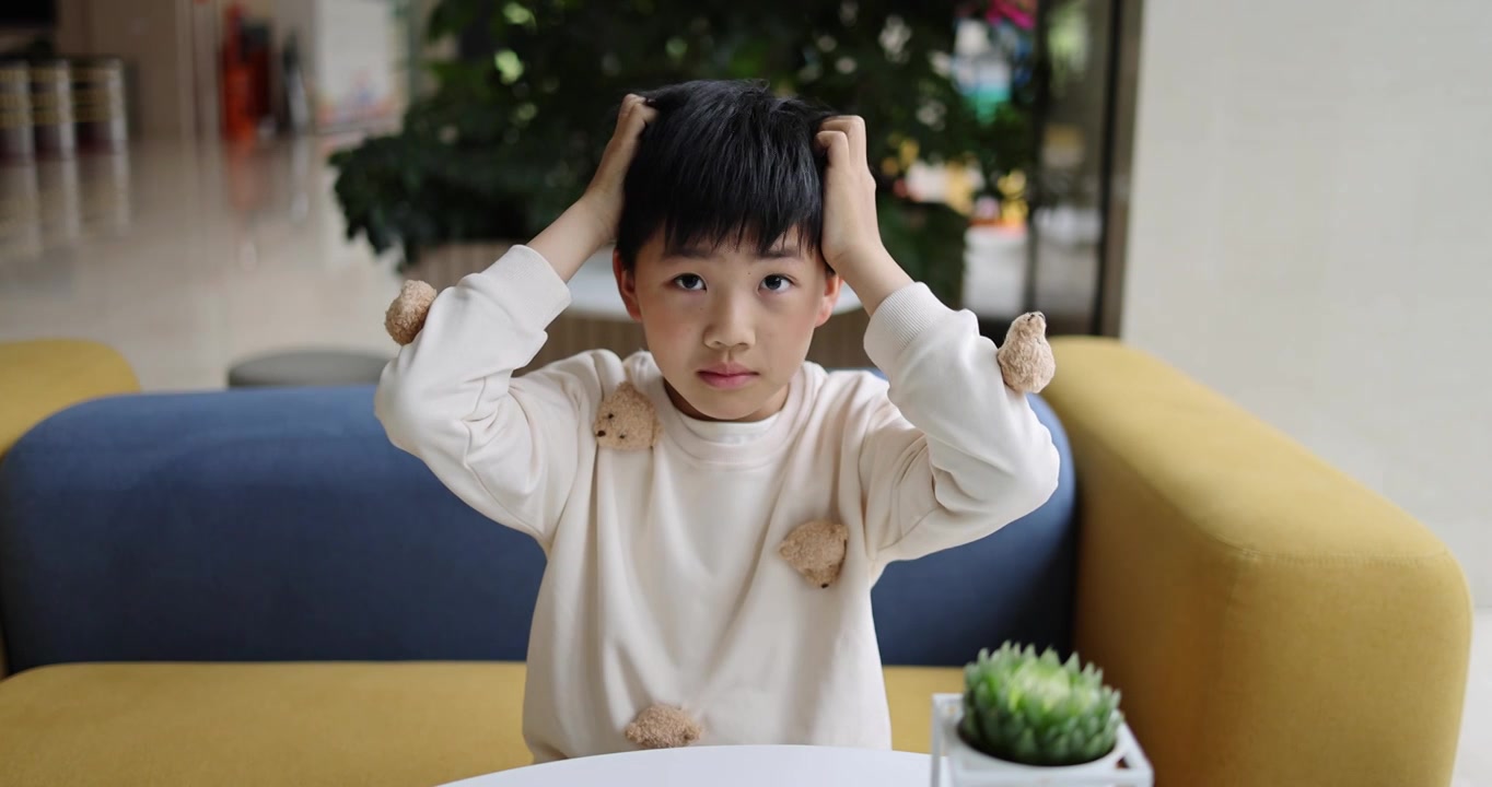 可爱的中国小男孩坐在沙发上抓头发视频下载