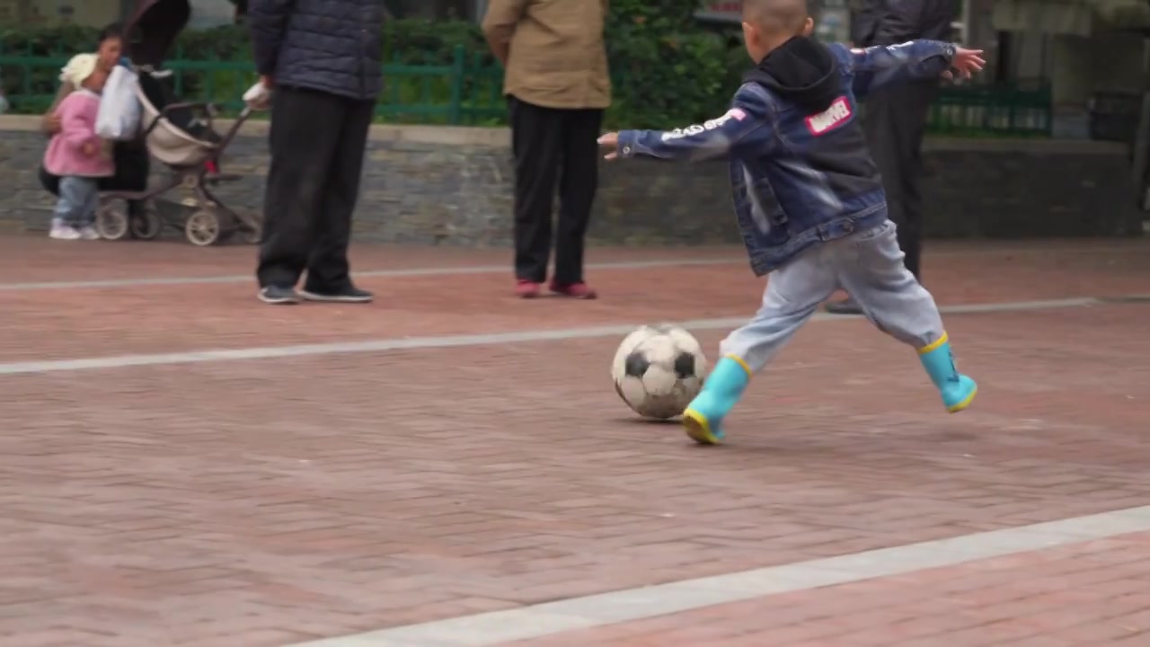 公园里一个穿着雨鞋的男性儿童在踢足球视频下载