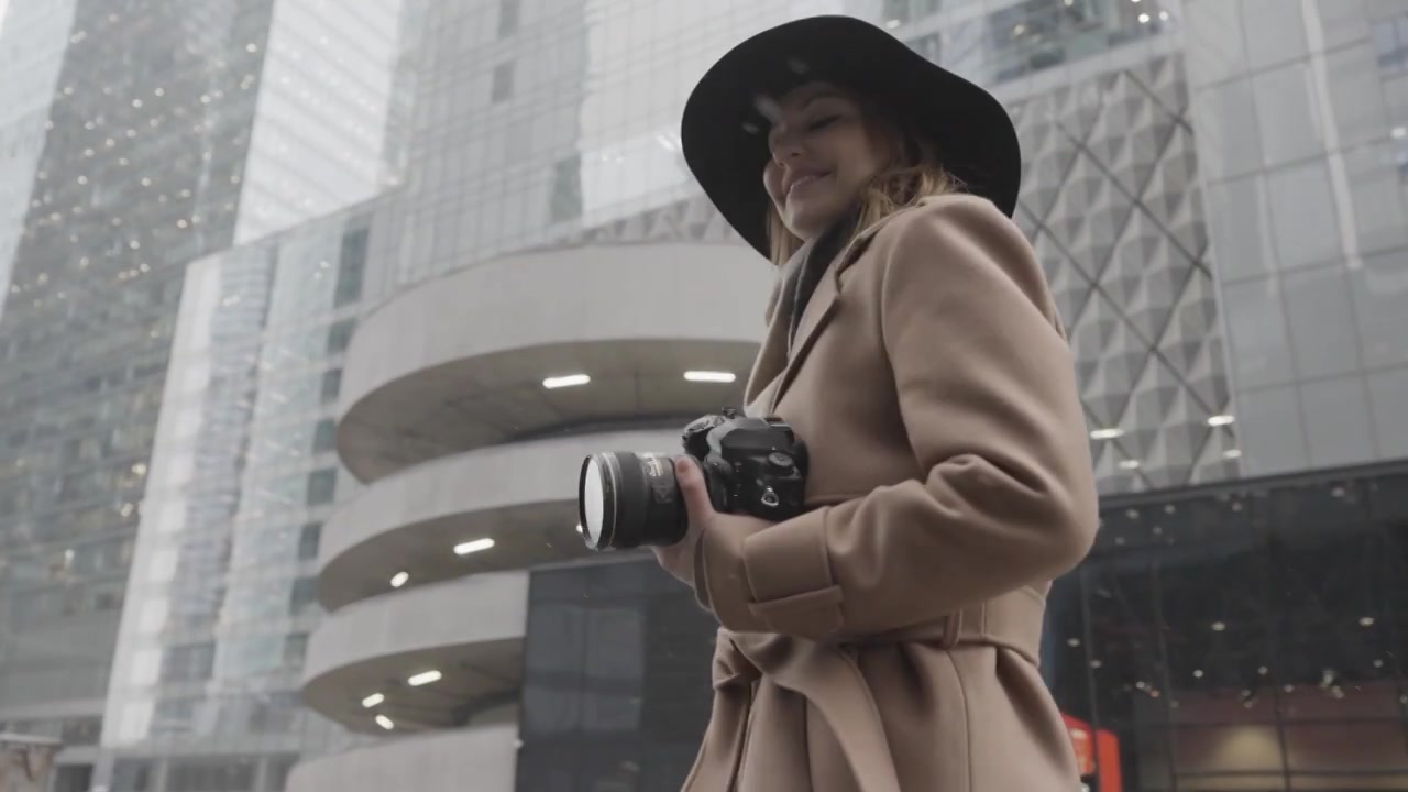 迷人的年轻金发女子手里拿着相机在城市的街道上视频下载