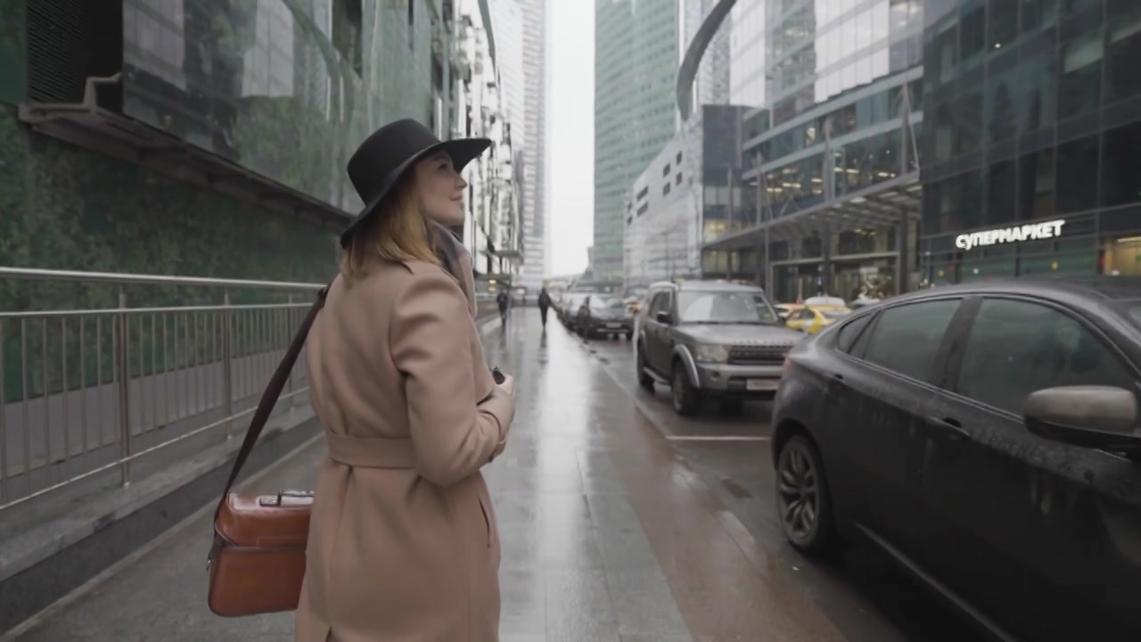 优雅的年轻女士穿着棕色的保暖外套，戴着黑色的帽子，高高走着视频下载