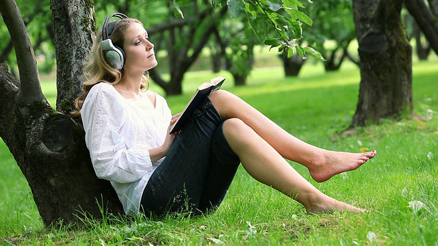 女人在公园里看书和听音乐视频素材