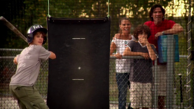 男孩在击球笼中击球，家人在一旁观看并为他加油视频素材