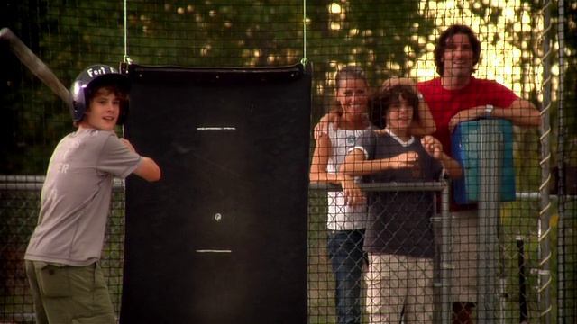 男孩在击球笼中击球，家人在外面观看他击球时为他欢呼视频素材