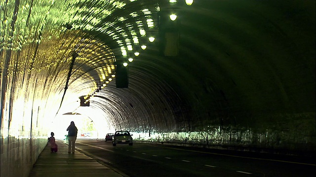 当车辆经过时，妇女和孩子走在隧道的人行道上/加州洛杉矶视频素材