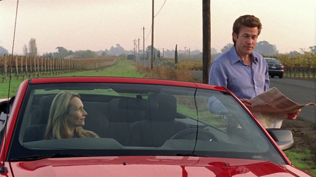 中景女人在红色敞篷车看地图，男人站在车外/女人给男人/纳帕谷，加利福尼亚视频素材