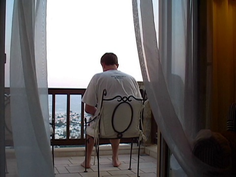 工作在窗帘后面。一名男子在阳台上使用笔记本电脑视频下载