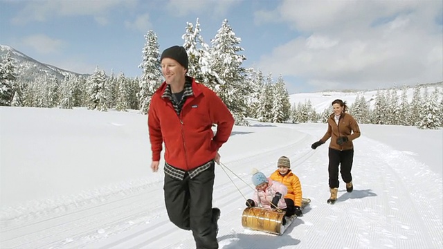 WS POV SLO MO父亲拉着两个孩子坐雪橇，母亲在后面跑/美国爱达荷州太阳谷视频素材