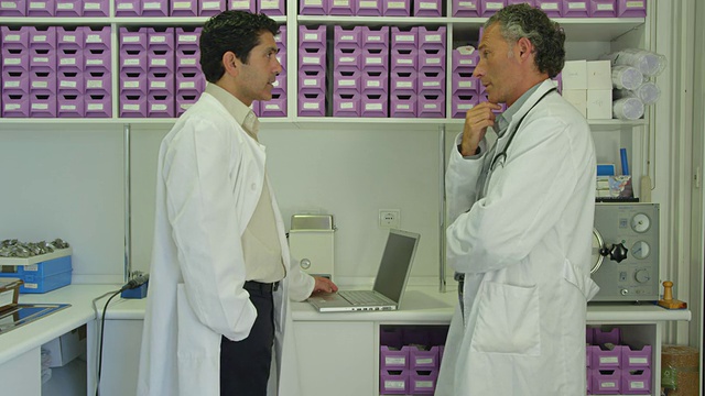 两位医生在实验室交谈，其中一位在笔记本电脑上打字视频下载