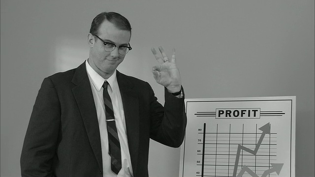 肖像商人站在显示利润增长的图表旁，竖起大拇指和OK标志，扣好夹克和直领带/纽约视频下载