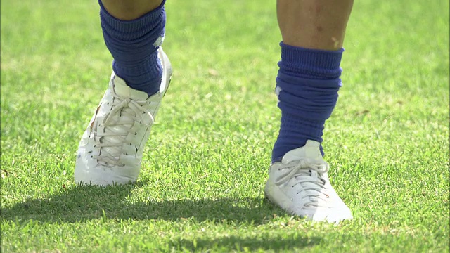 中近距手持式-穿着球鞋的脚在草地上反复踢足球视频下载