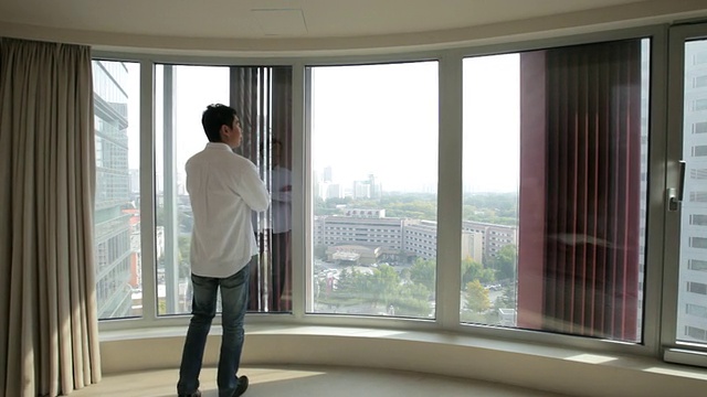 中国北京，一名年轻男子从公寓窗口望着窗外的景色视频下载