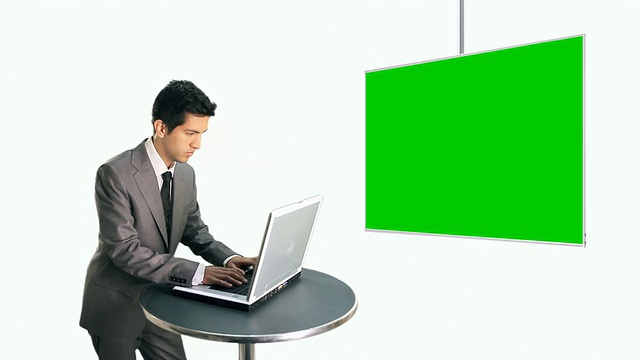 商人在笔记本电脑上打字，看着一个大屏幕视频素材