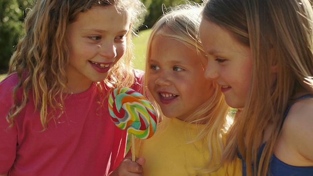 三个孩子在公园里舔棒棒糖的照片。视频下载