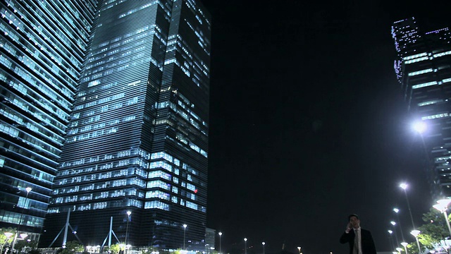 新加坡，MH LA LD商人在电话中行走和交谈，夜间灯光照亮的建筑背景视频素材