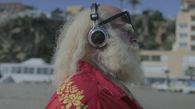 白色长发(圣诞老人)，胡须，夏威夷衬衫，戴着耳机听音乐的大个子男人视频素材