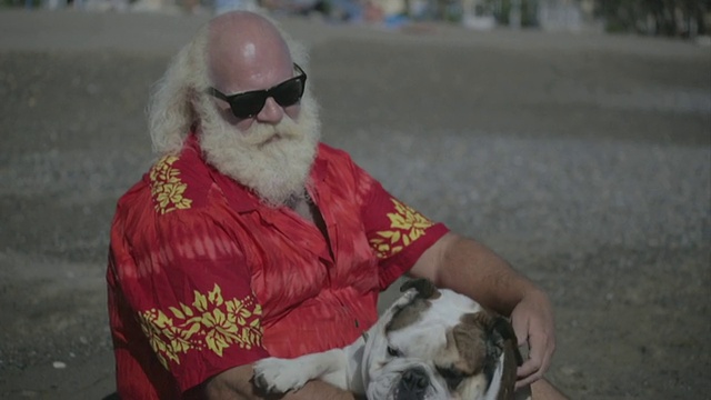白色长发(圣诞老人)，胡子，和夏威夷衬衫在海滩上看着海浪视频素材