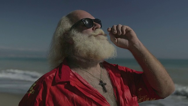 白色长发(圣诞老人)，胡子，太阳镜和夏威夷衬衫的大个子男人在海滩上视频素材