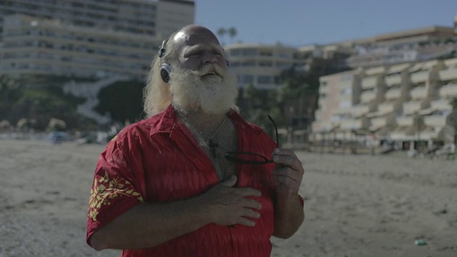 白色长发(圣诞老人)，胡子，夏威夷衬衫，耳机，在海滩上视频素材