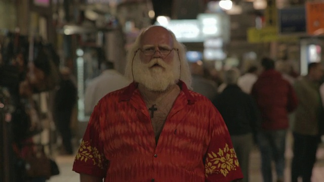M/S to C/U白色长发(圣诞老人)，胡子，夏威夷衬衫，走在商业街上的夜晚视频素材