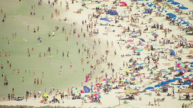 美国佛罗里达州的清水海滩，成群的海滩游客穿着泳衣，撑着雨伞从水里出来视频下载