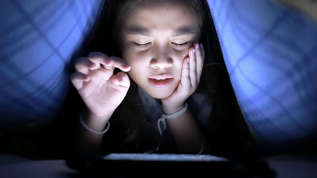 小女孩在毯子下面用平板电脑视频素材