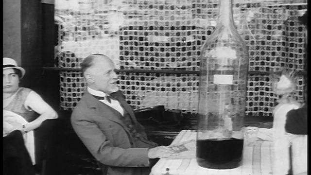 在户外咖啡馆/巴黎/纪录片中，20世纪20年代的服务生给餐桌上的男人端来了一大瓶葡萄酒视频下载