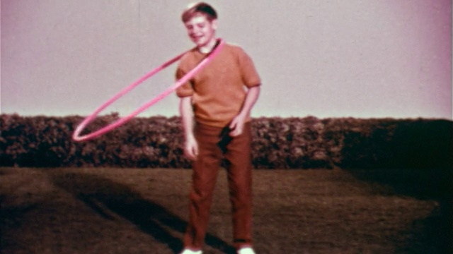 1959年慢镜头男孩站在草坪上，身体上绕着塑料圈，脖子上绕着圈视频下载