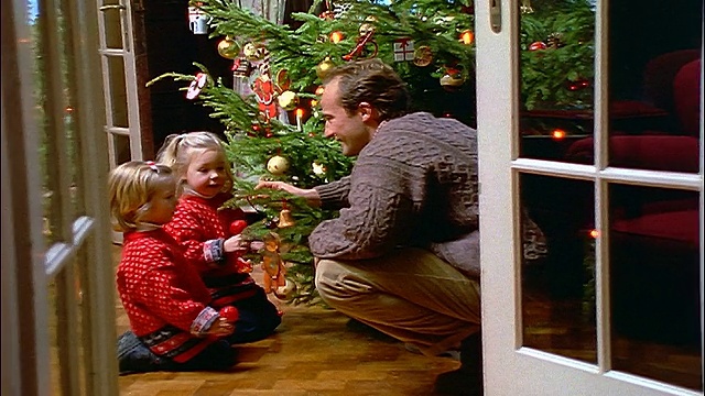 摄影车拍到父亲在圣诞树旁和两个金发小女孩说话视频素材