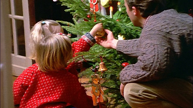 缩小镜头，拍摄父亲和两个金发小女孩装饰圣诞树视频素材