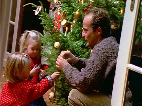 娃娃拍下了爸爸和两个装饰圣诞树的金发小女孩视频素材