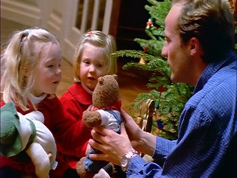 CANTED摄影车拍摄了两个金发小女孩和父亲在圣诞树旁玩毛绒玩具视频素材