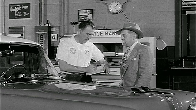 20世纪50年代，一名男子在车库里与正在车旁写作的机械师交谈视频下载